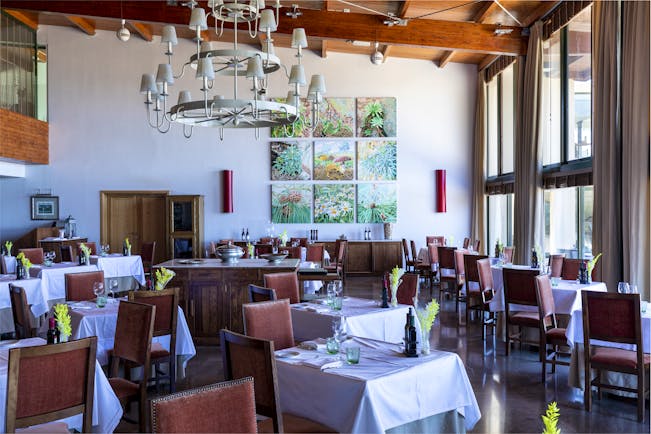 Restaurant with large chandelier, lots of tables and chairs set out for dining and art work on the walls