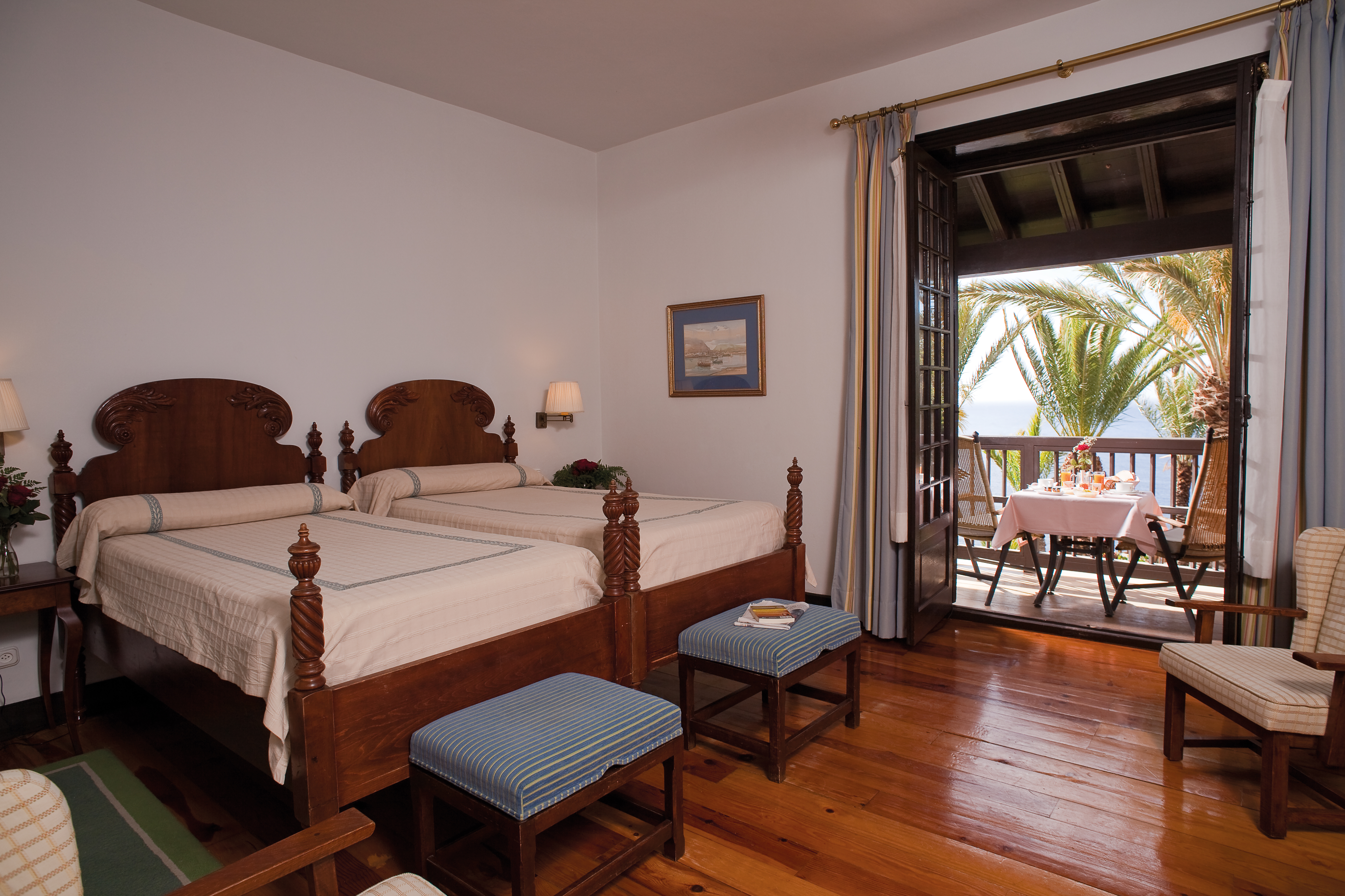 Twin bedroom with two double beds and double doors opening up onto a balcony with seating area