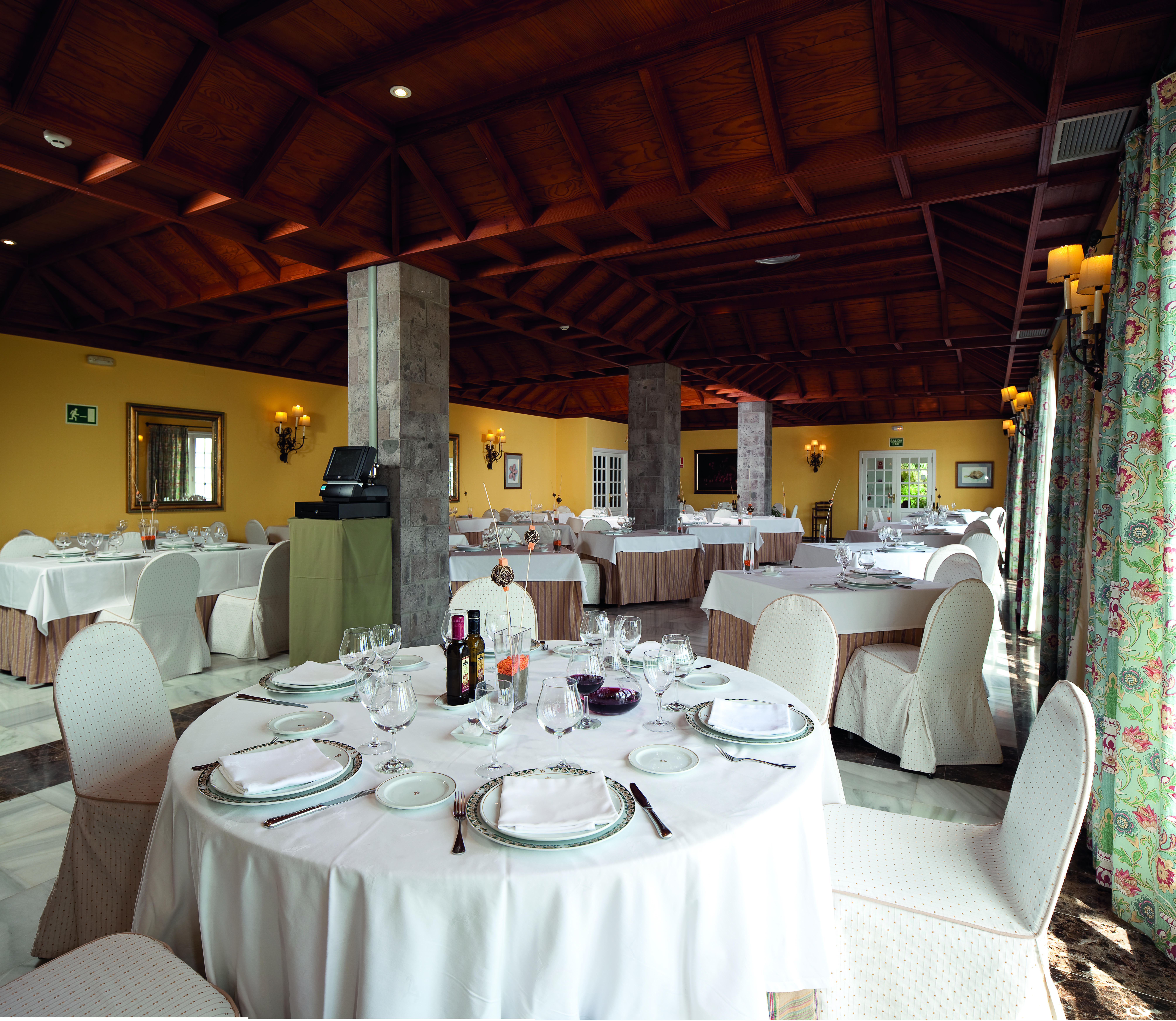 Restaurant with dining tables set out with wood pannelled ceilings and stone pillars