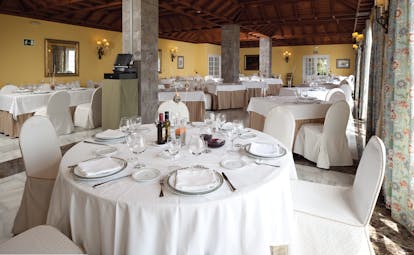 Restaurant with dining tables set out with wood pannelled ceilings and stone pillars