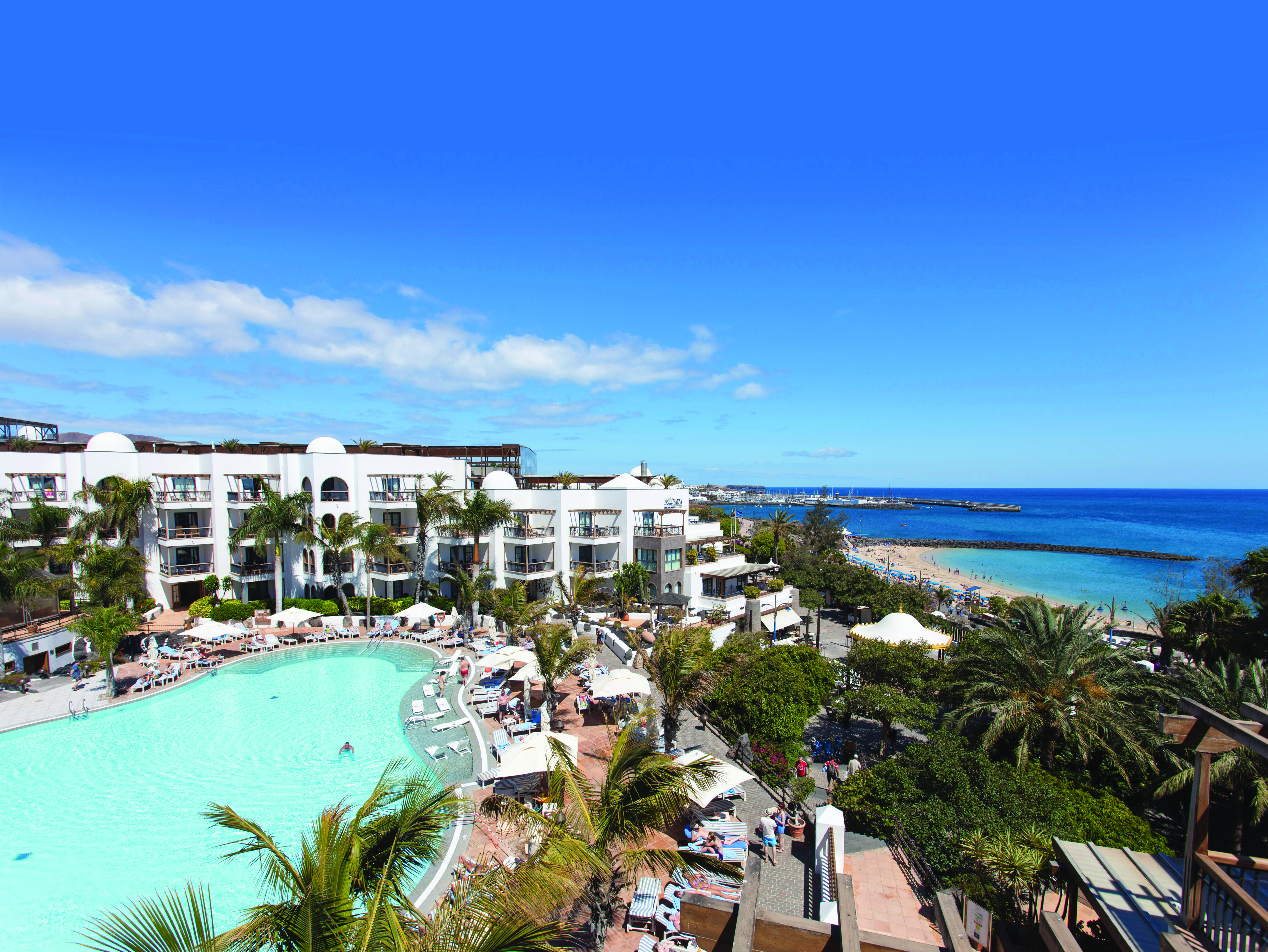 Princesa Yaiza pool aerial shot, beach and sea in background, hotel buildings, pool deck, sun loungers, palm trees