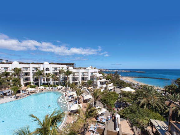 Princesa Yaiza pool aerial shot, beach and sea in background, hotel buildings, pool deck, sun loungers, palm trees