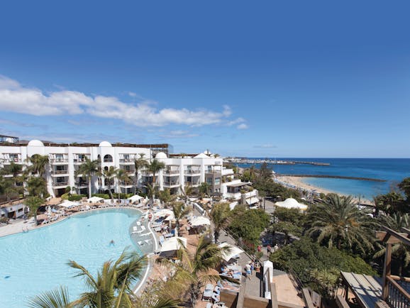 Princesa Yaiza pool aerial shot, beach and sea in background, hotel buildings, pool deck, sun loungers, palm trees