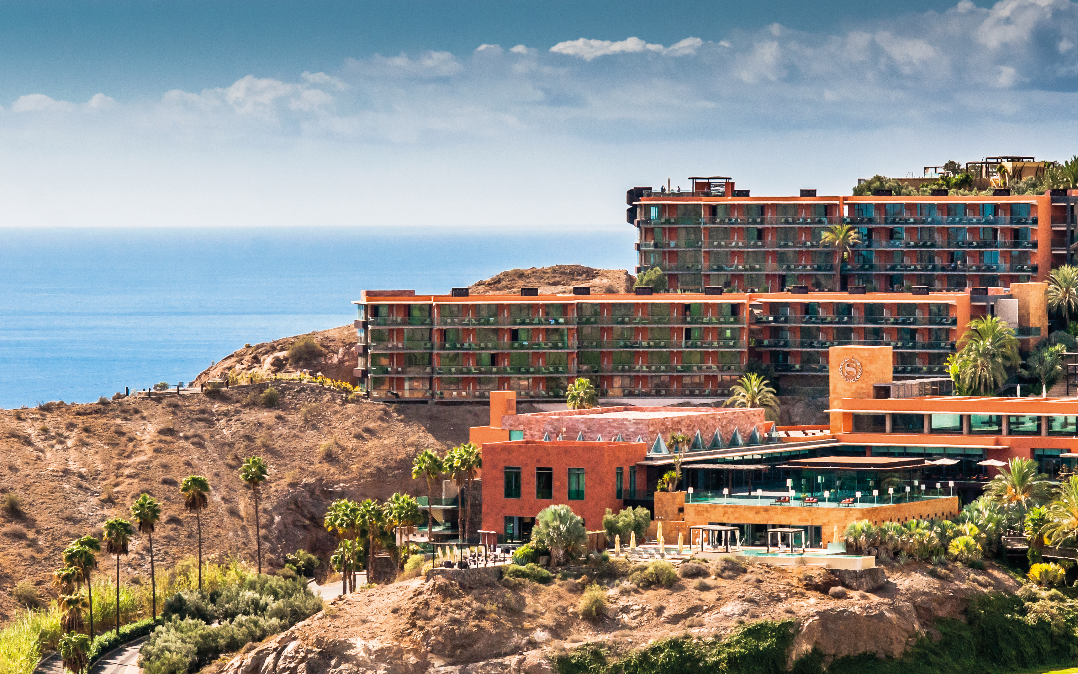 Exterior of hotel buildings amongst hills looking out over the sea