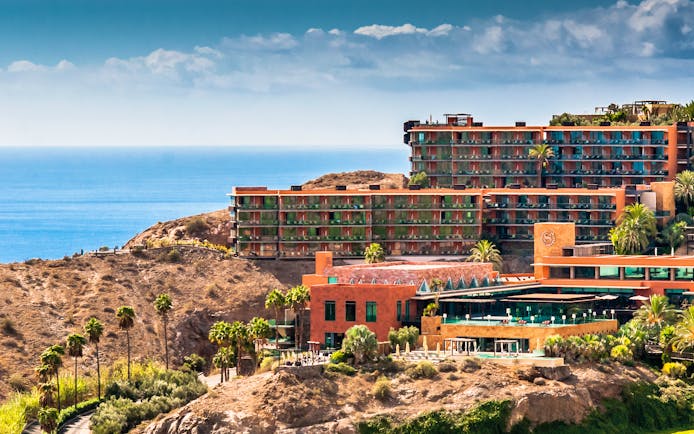 Exterior of hotel buildings amongst hills looking out over the sea