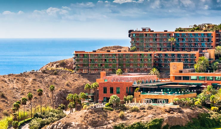 Exterior of hotel buildings amongst hills looking out over the sea