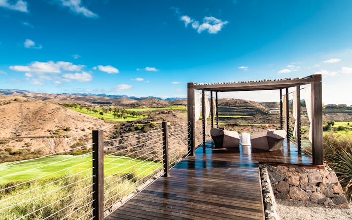 Golf viewing area with wood pannelled bridge, seating area covered by a porch and view of the golf course