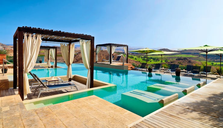 Outdoor pool with cabanas and sun beds around the outskirts of the pool