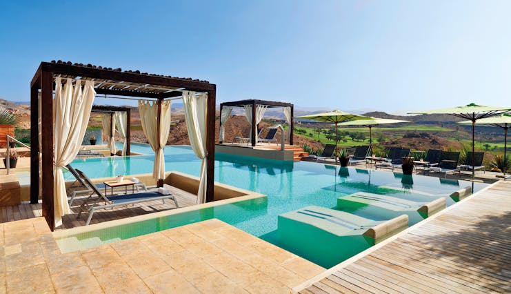 Outdoor pool with cabanas and sun beds around the outskirts of the pool