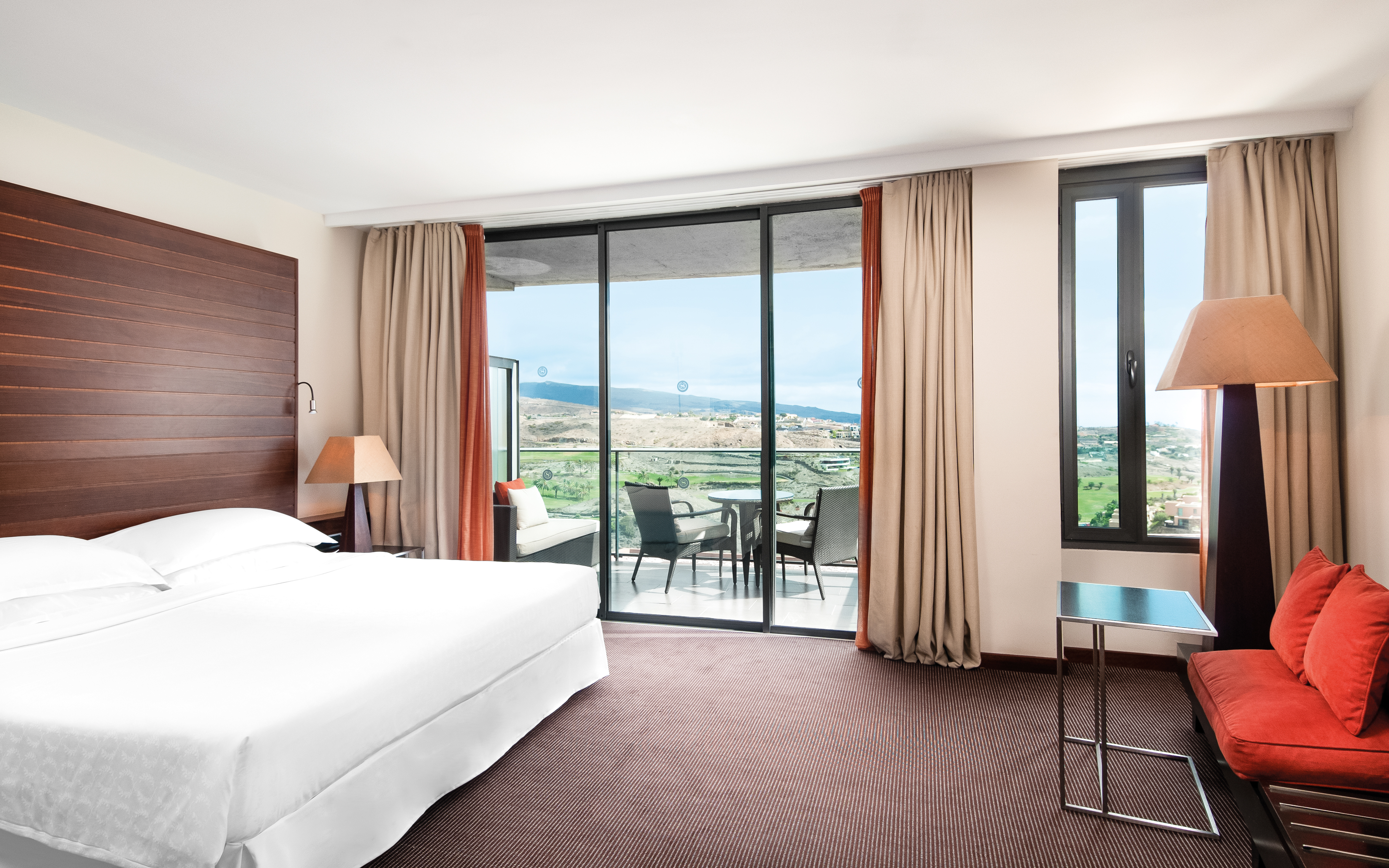 Premiere bedroom with large double bed, doors opening onto a terrace balcony with seats on 