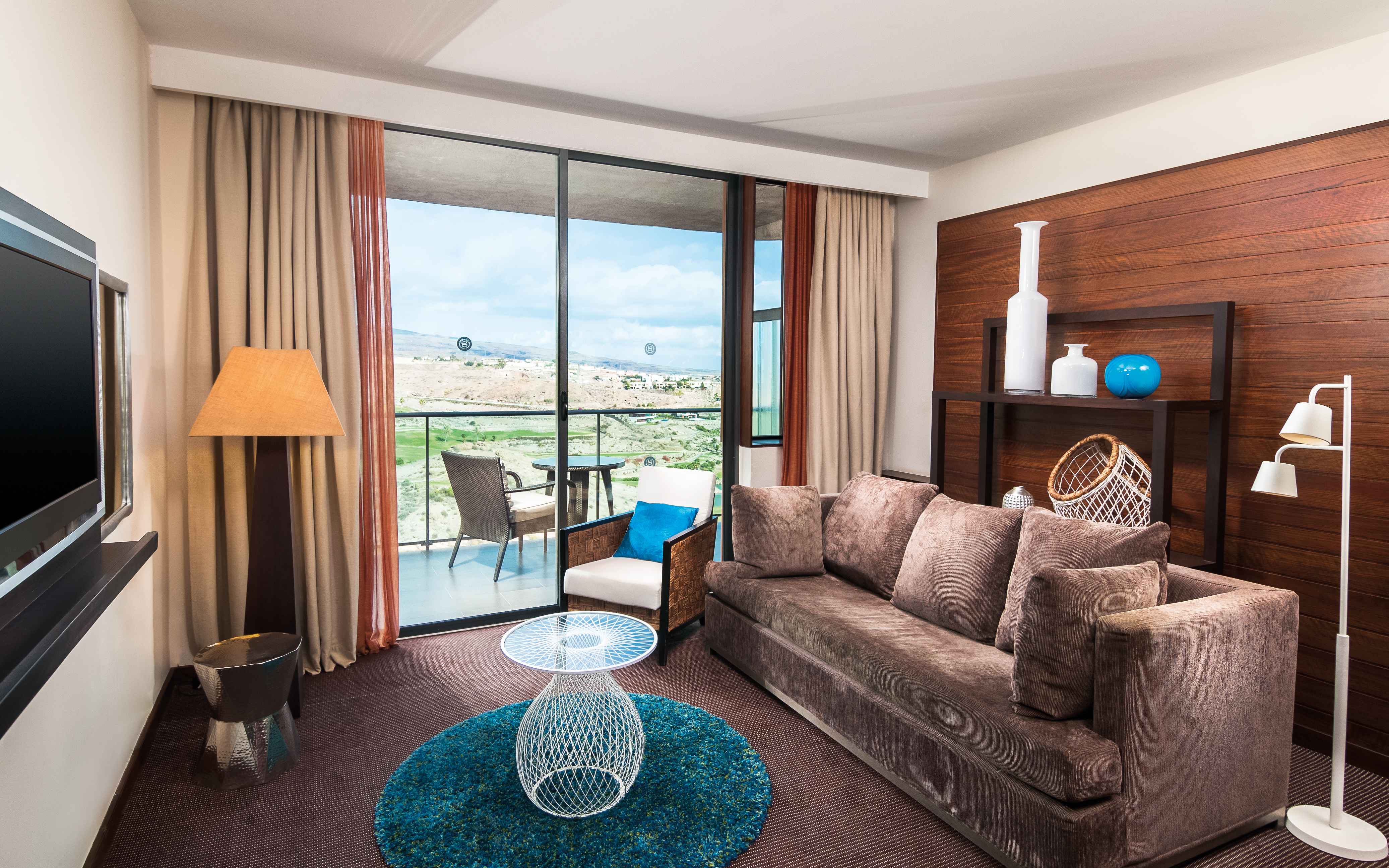 Suite living room with large velvet sofa, television and doors opening onto a terrace balcony
