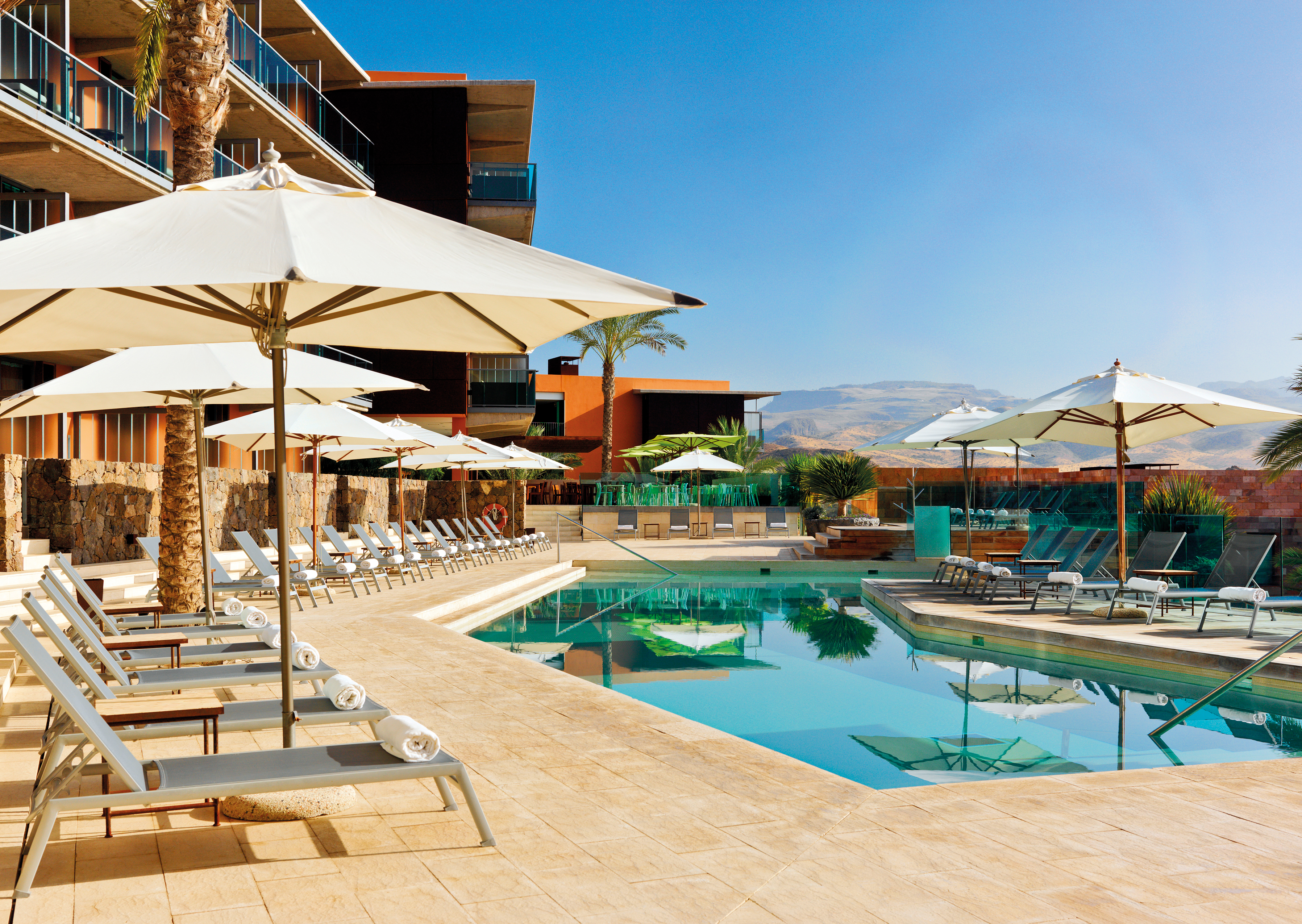 Swimming pool with sun loungers and umbrellas set up around the edge of the pool 
