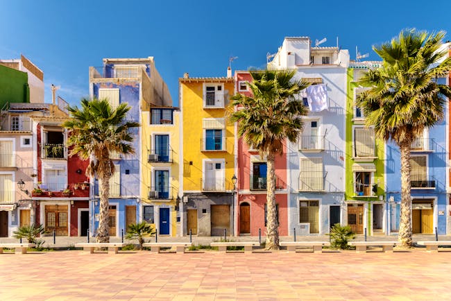 Narrow houses on the beach lined with palms painted bright colours with shutters at Villajoyosa near Alicante