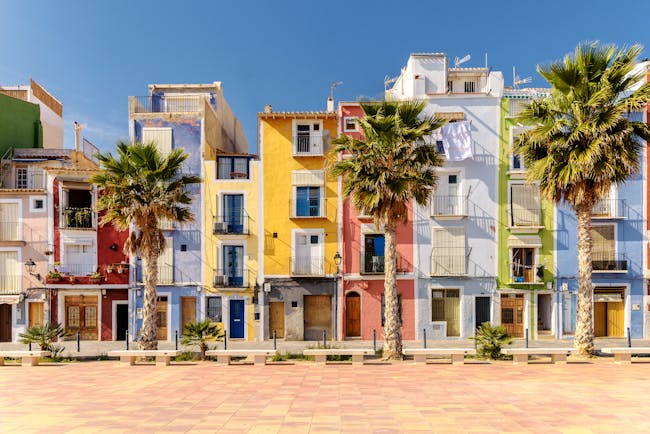 Narrow houses on the beach lined with palms painted bright colours with shutters at Villajoyosa near Alicante