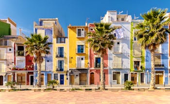 Narrow houses on the beach lined with palms painted bright colours with shutters at Villajoyosa near Alicante