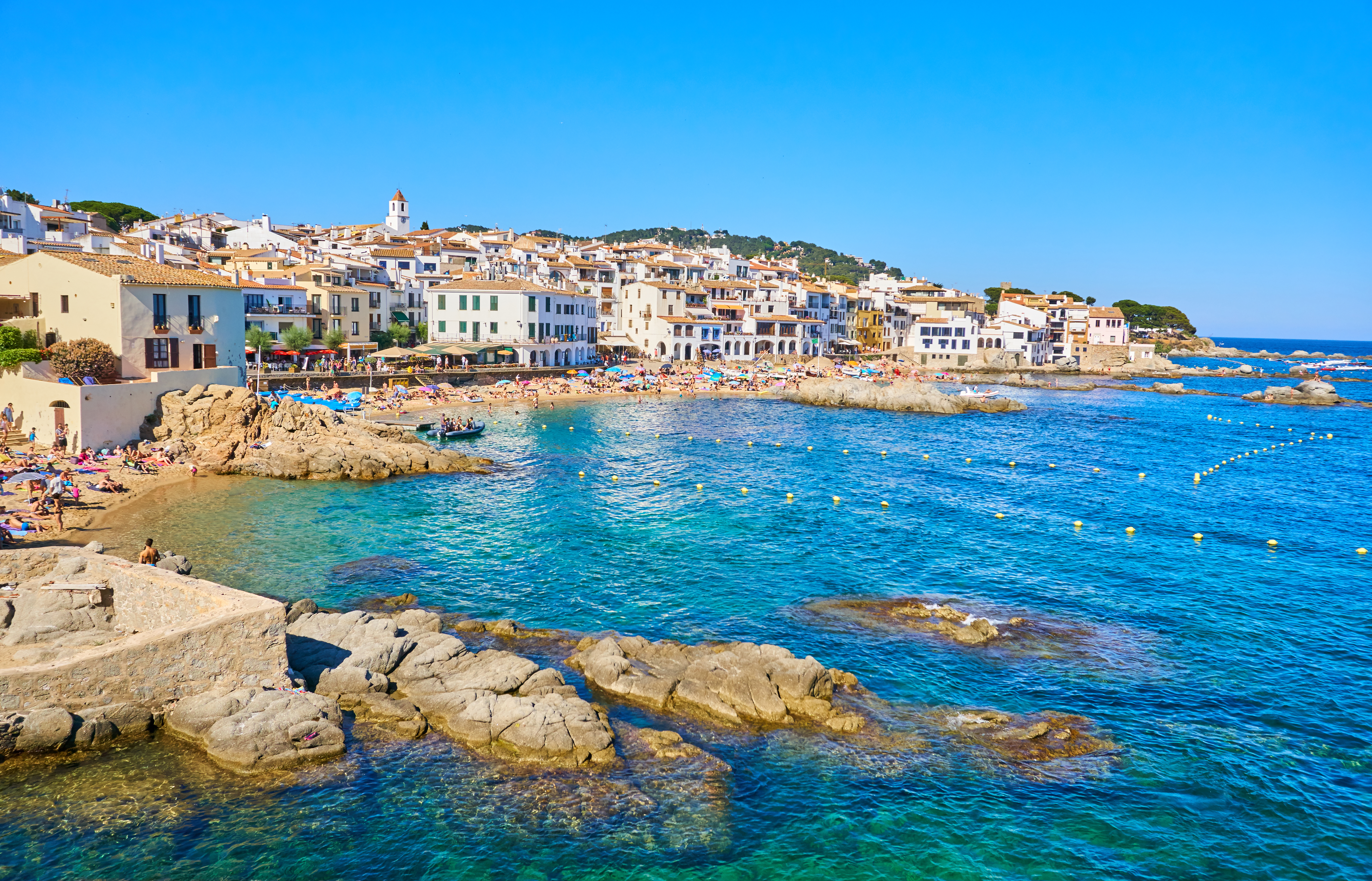 Blue sea lapping rounded rocks on coast with village behind at Palafrugell in Catalonia