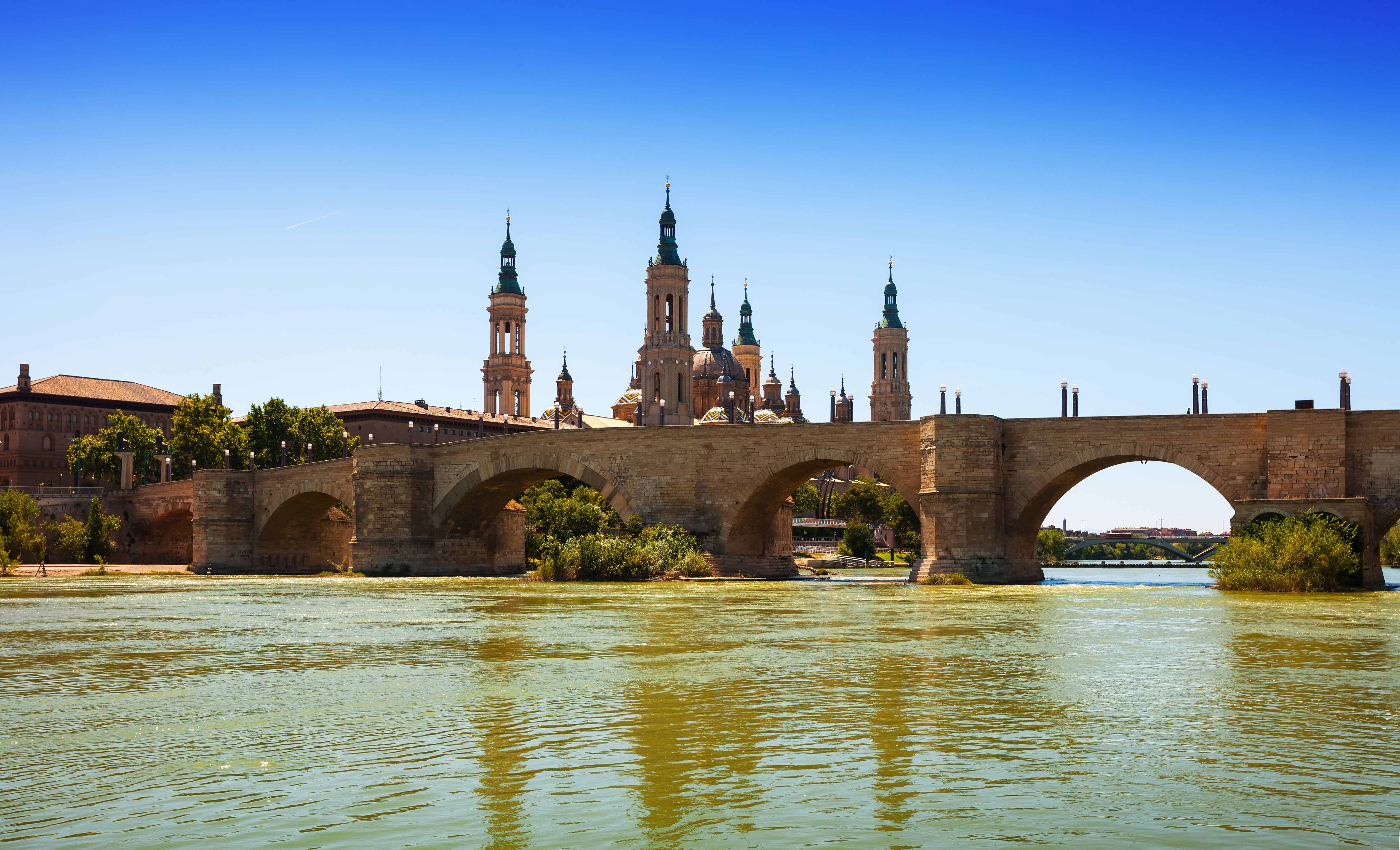 Stone bridge over wide river with the skyline dominated by the ornate spires of Zaragoza cathedral