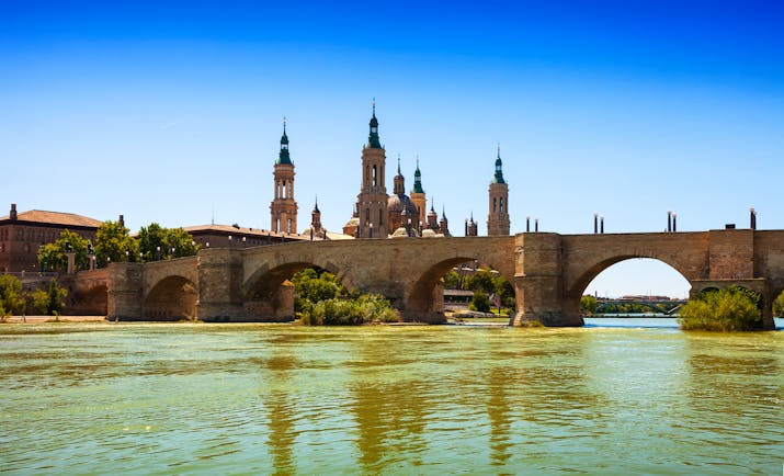 Stone bridge over wide river with the skyline dominated by the ornate spires of Zaragoza cathedral