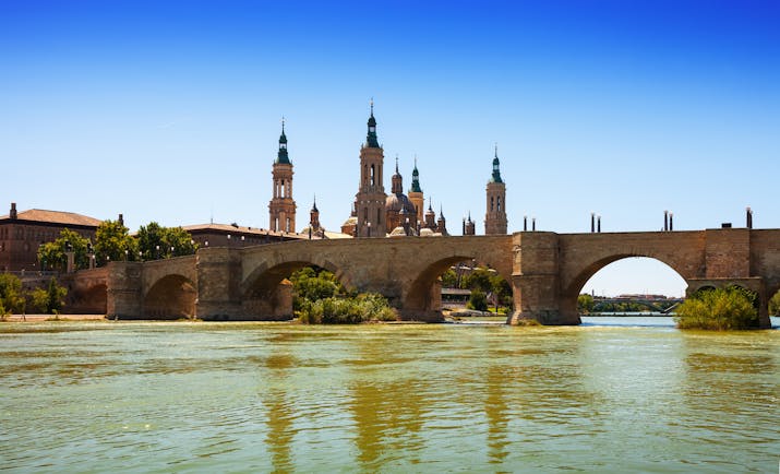 Stone bridge over wide river with the skyline dominated by the ornate spires of Zaragoza cathedral