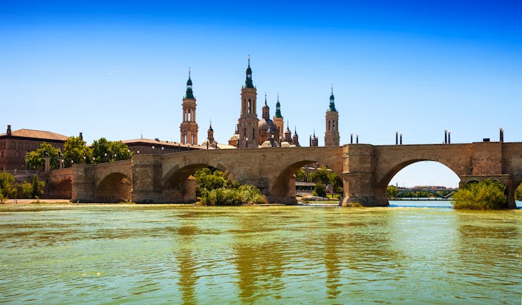 Stone bridge over wide river with the skyline dominated by the ornate spires of Zaragoza cathedral