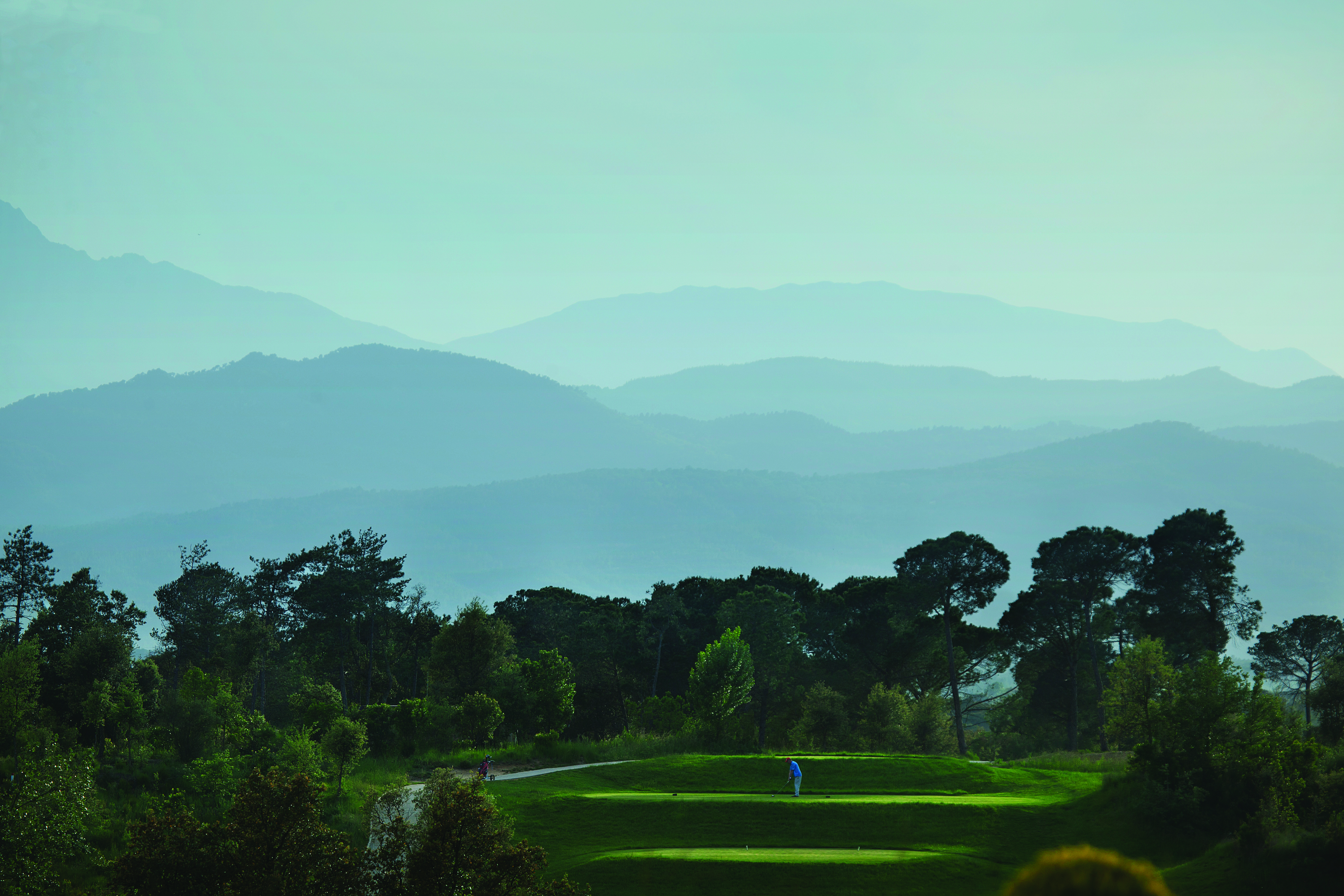 Hotel Camiral golf course, putting green surrounded by trees, mountains in background
