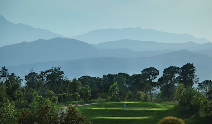 Hotel Camiral golf course, putting green surrounded by trees, mountains in background