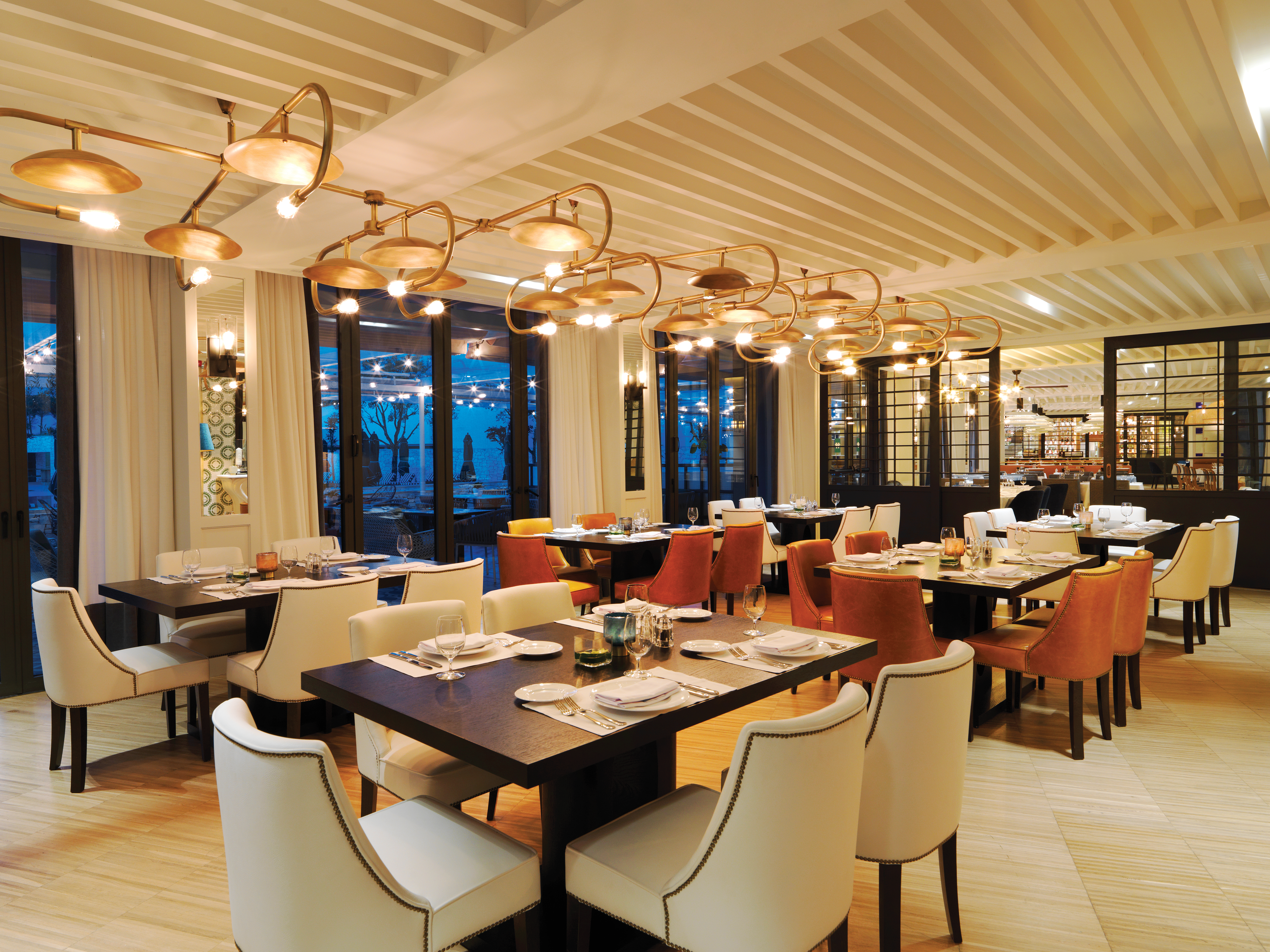 Hotel restaurant with tables and chairs set up for dining with chandeliers hanging from ceiling
