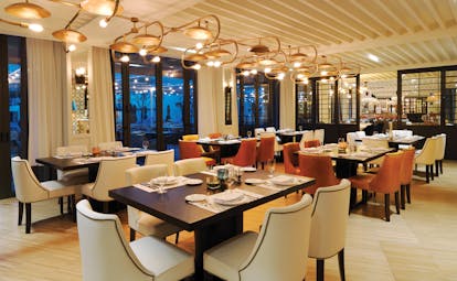 Hotel restaurant with tables and chairs set up for dining with chandeliers hanging from ceiling