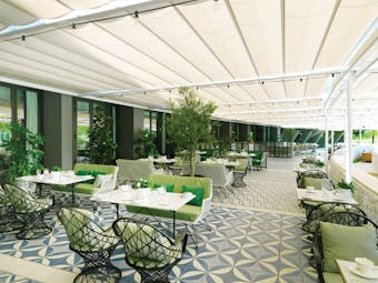 Terrace with veranda overhead, tables set out for dining and plants scattered around