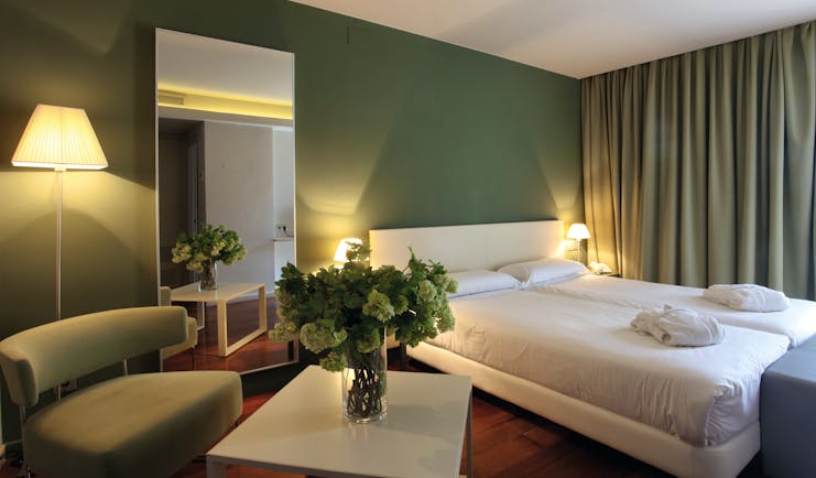 Another bedroom at the Hotel Gran Claustre with a large double bed, sofa, flowers on the desk and a green colour scheme