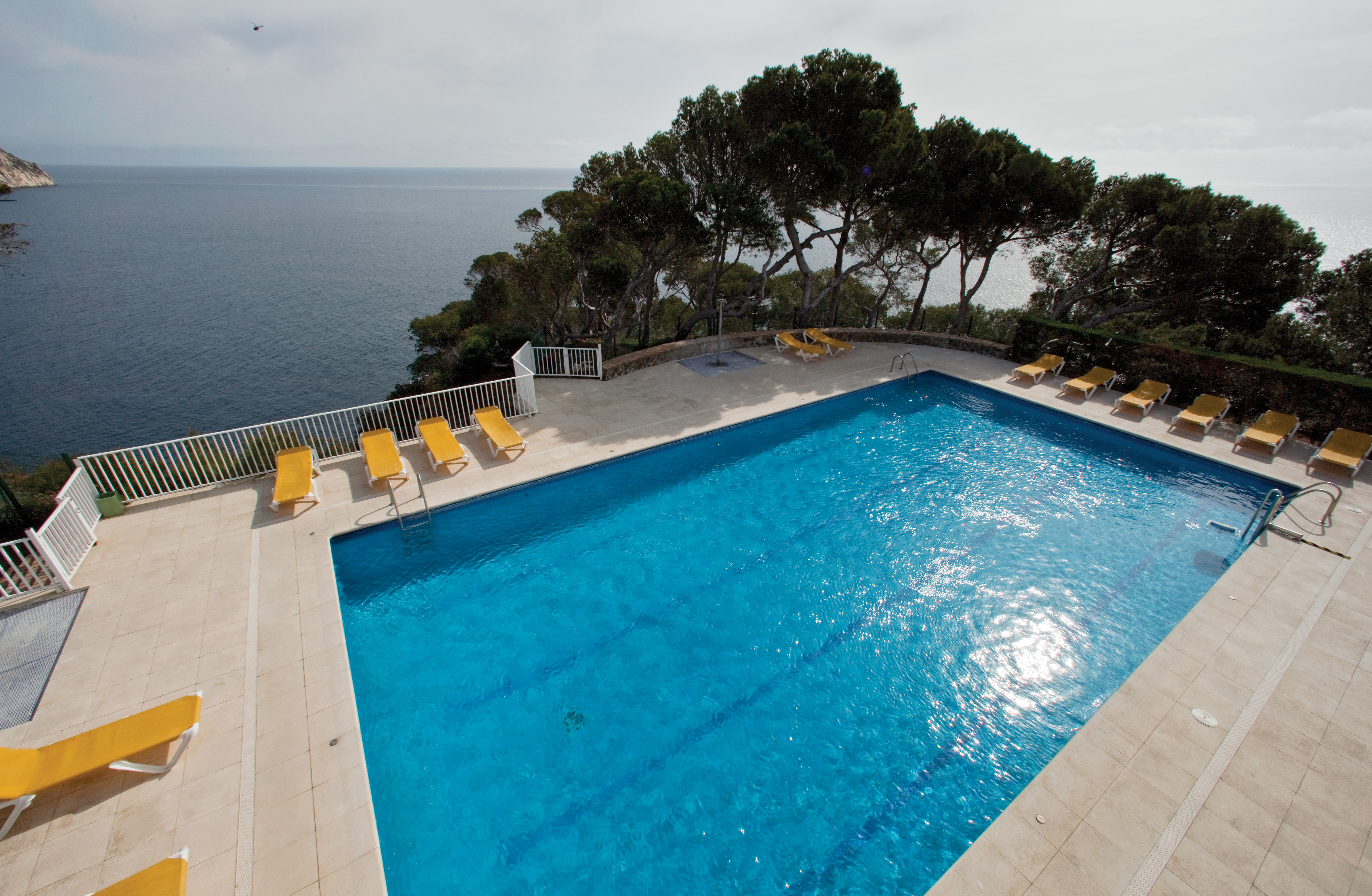 Outdoor pool with yellow sun loungers surrounding the pool and the sea in the background