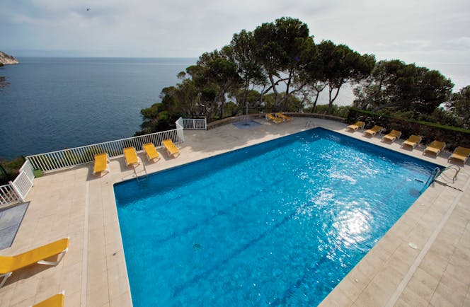 Outdoor pool with yellow sun loungers surrounding the pool and the sea in the background