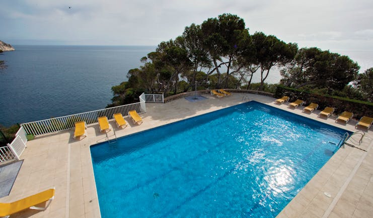 Outdoor pool with yellow sun loungers surrounding the pool and the sea in the background