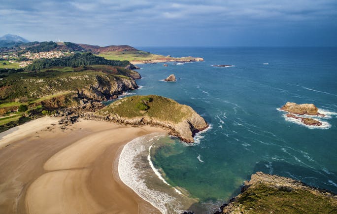 Sweep of golden sand beach with cliffs and headland in distance at Llanes in Asturias