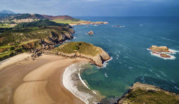 Sweep of golden sand beach with cliffs and headland in distance at Llanes in Asturias