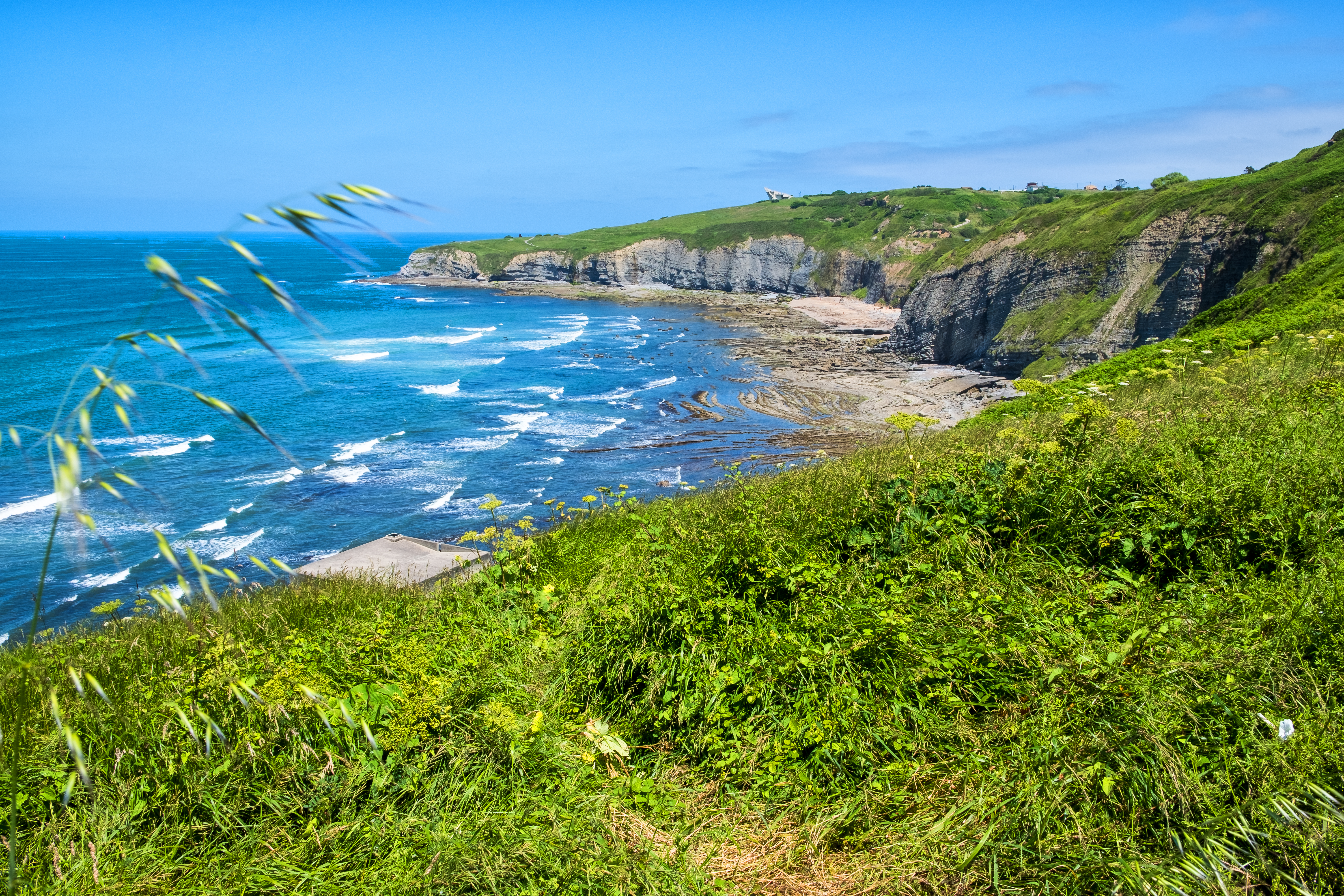 Surf crashing onto deserted beach at bottom of grey and green cliffs in Gijon Asturias