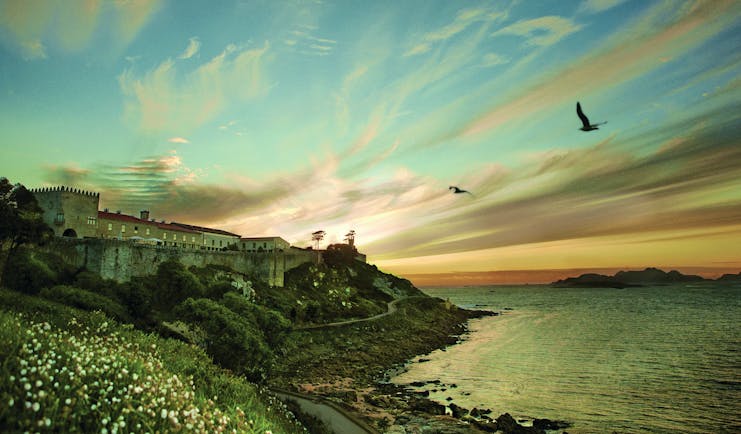 Parador de Baiona Green Spain view of hotel nestled in the cliffside beach in foreground