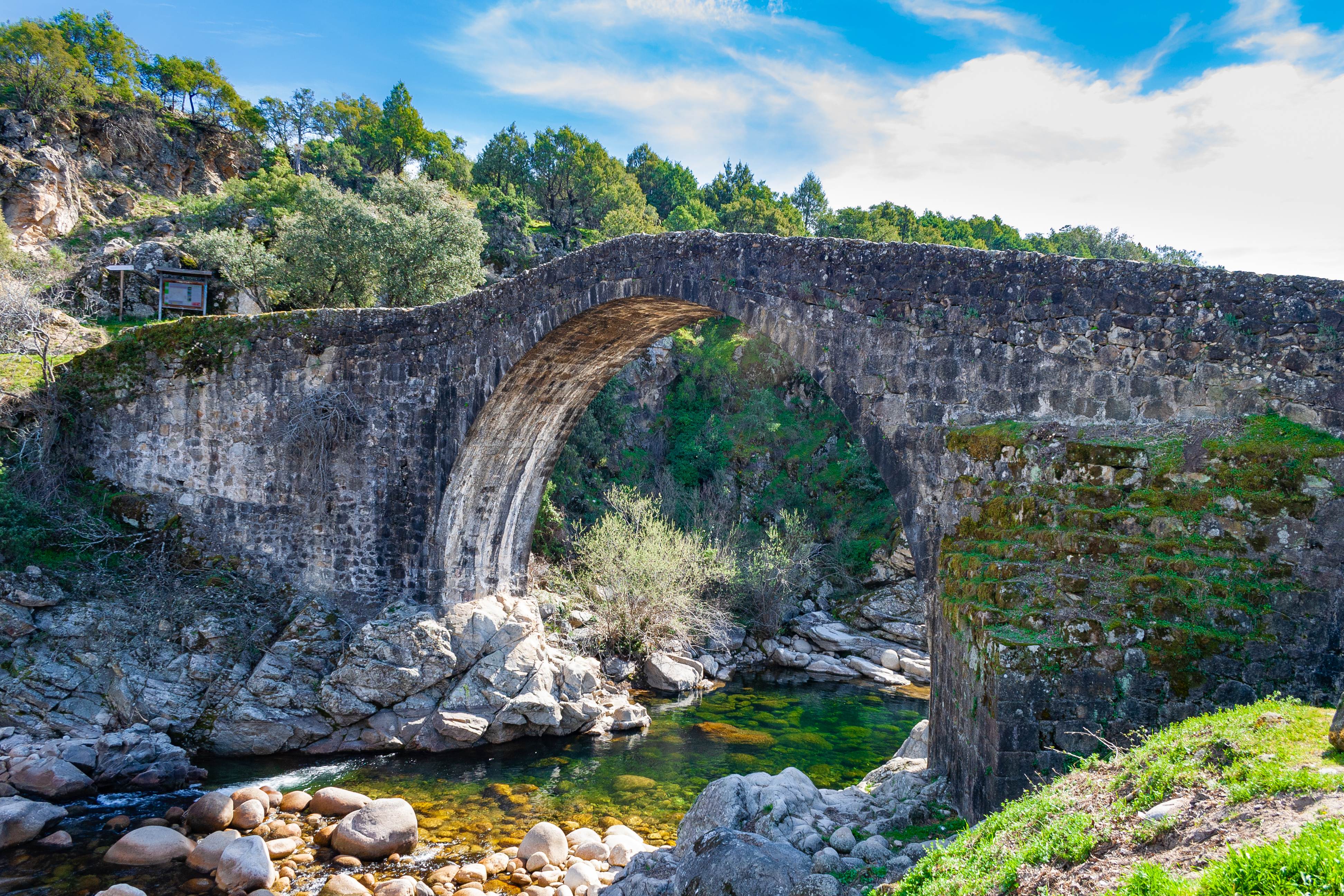 Old stone bridge over small river with rocks below and cliffs behind in the Sierra de Gredos Extremadura
