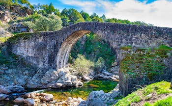 Old stone bridge over small river with rocks below and cliffs behind in the Sierra de Gredos Extremadura