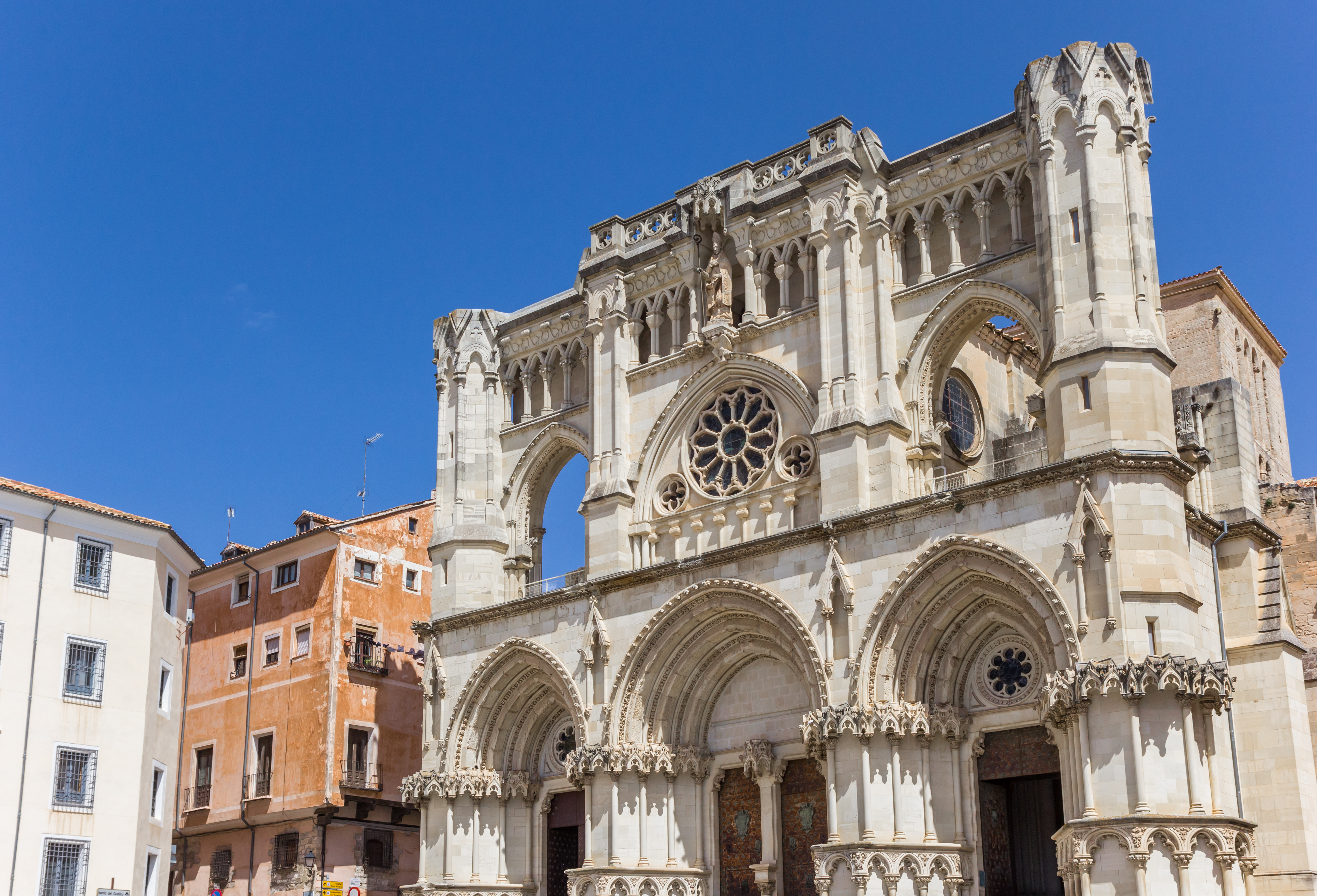 Pale stone facade richly sculpted with rose window and statue of bishop at the Cathedral of Cuenca