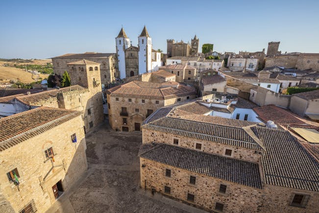 Stone buildings with tiled roofs and white and brown church with towers in Caceres