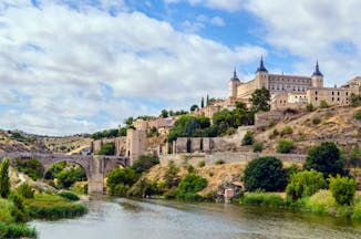 River in foreground with the square shape of the alcazar of Toledo on the hilltop above the city