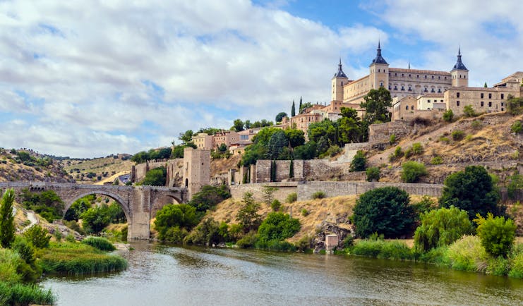 River in foreground with the square shape of the alcazar of Toledo on the hilltop above the city