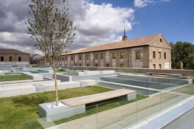 Parador de Alcala de Henares gardens, lawns, trees, hotel buildings, modern garden benches