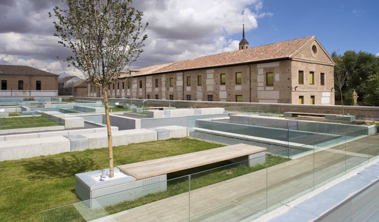 Parador de Alcala de Henares gardens, lawns, trees, hotel buildings, modern garden benches