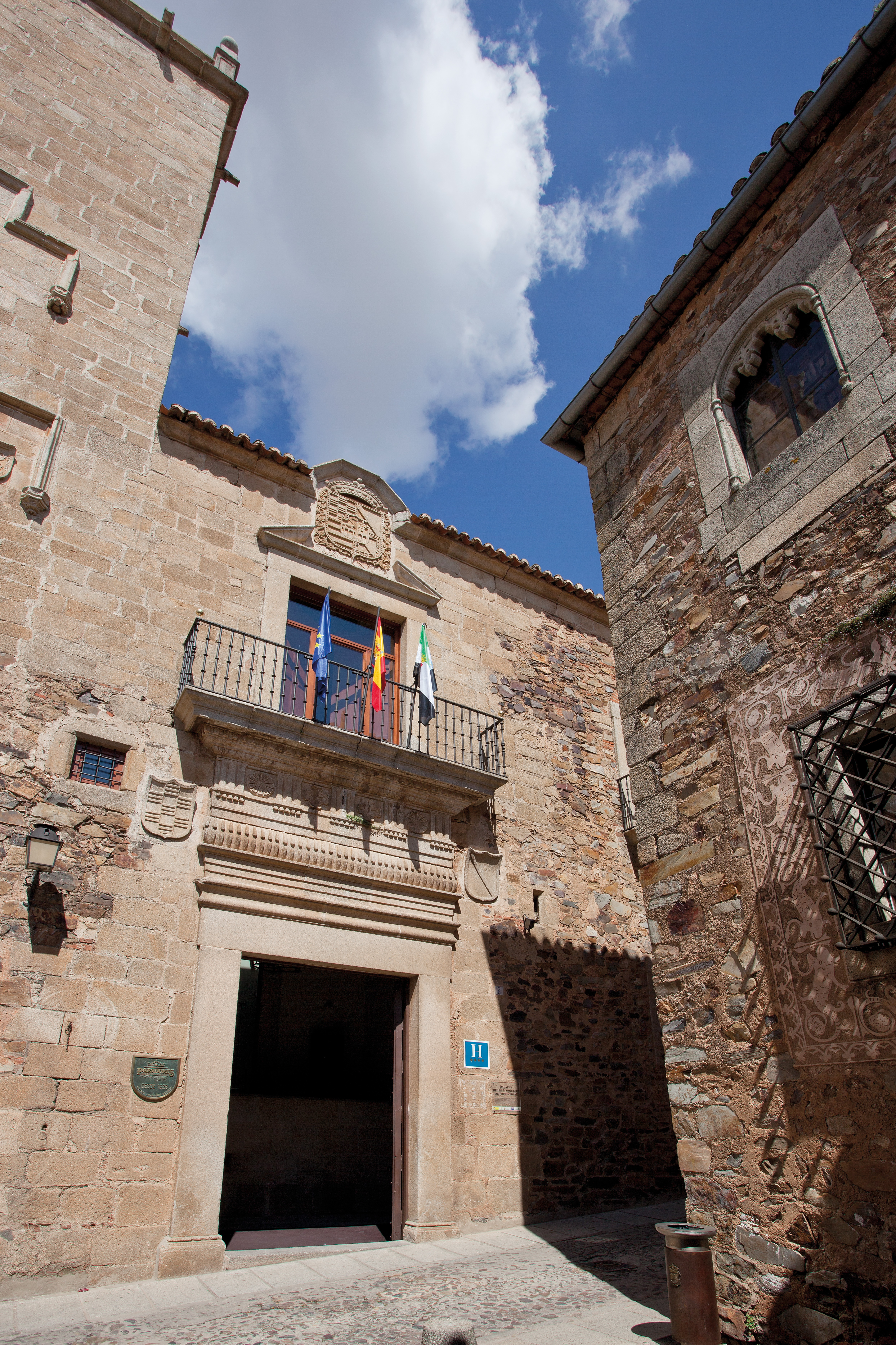 Entrance to hotel with large doorway with balcony above with flags on it