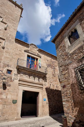 Entrance to hotel with large doorway with balcony above with flags on it
