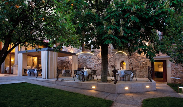 Outdoor dining terrace with tables and chairs set out shaded by a large tree