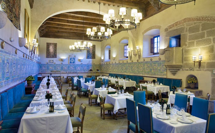 Restaurant with tables and blue chairs set out for dining and chandeliers hanging from the ceiling