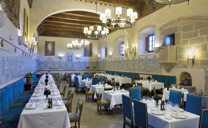 Restaurant with tables and blue chairs set out for dining and chandeliers hanging from the ceiling